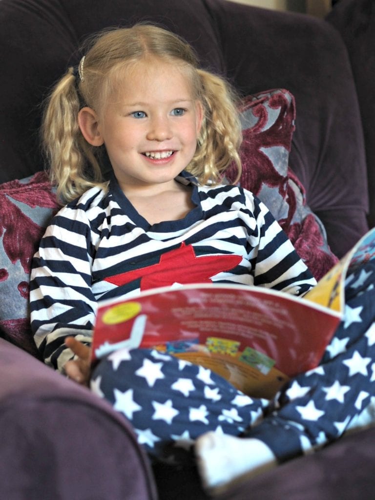 Is Tech Replacing Story Time for Families? Help the Book Trust on the 7th June. Aria sitting in an armchair, in her pjs, reading a book