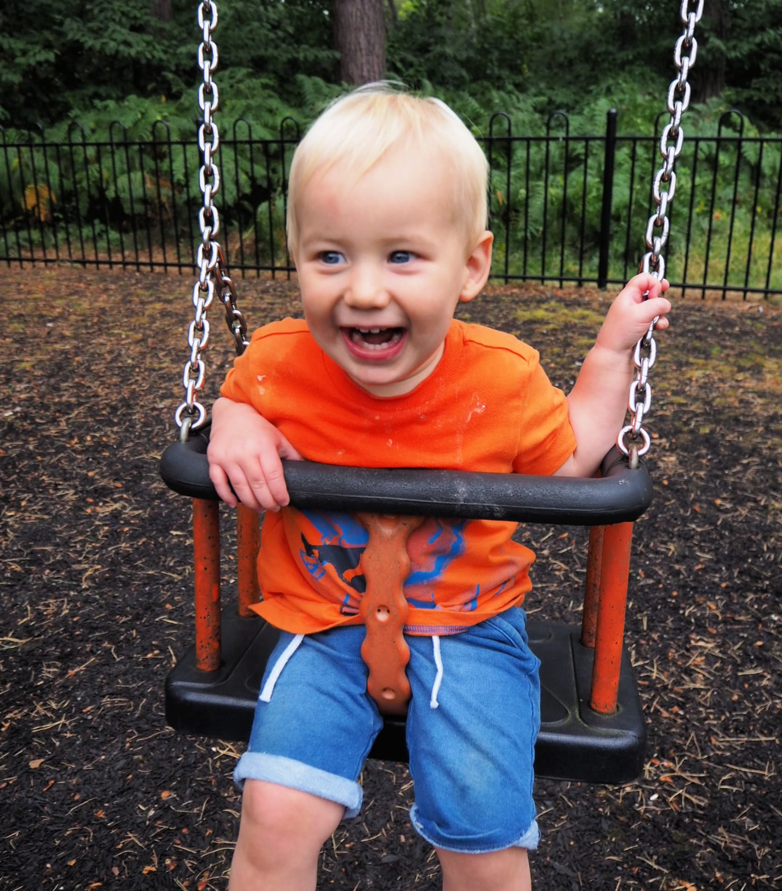 Bodhi at 15 Months - Bodhi swinging on the swings in an orange t-shirt