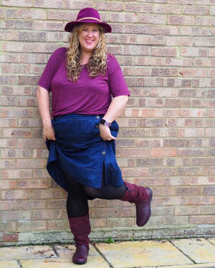 Me wearing a hat, maroon top and denim skirt in a pair of maroon hotter boots kicking one leg up to the side