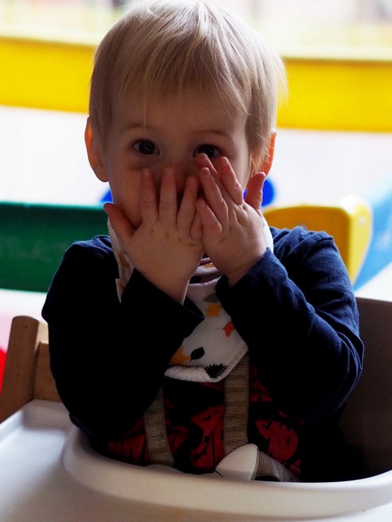 A little boy in his highchair playing peekabo