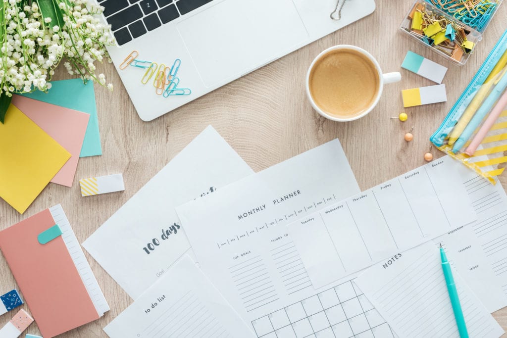 picture of desk with laptop, cup of coffee, and planning notes and stationery