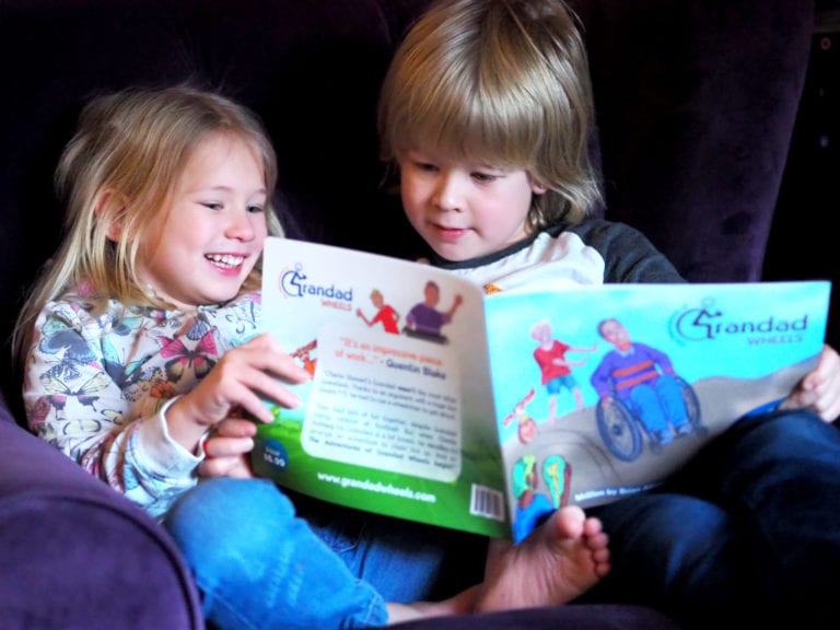 Logan and Aria sat on in an arm chair reading Grandad Wheels