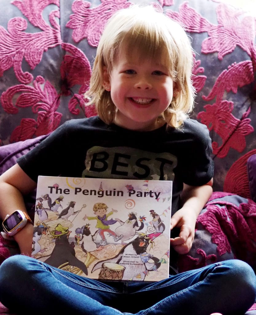 The penguin party book review - Logan sitting on the sofa smiling with the book