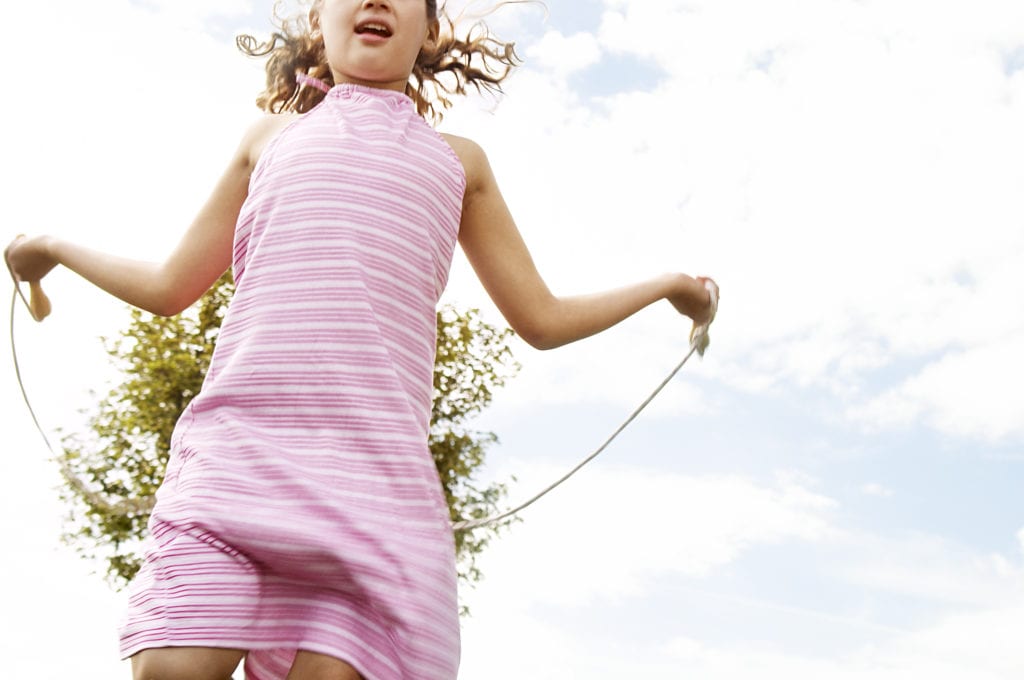 How to Keep Active When Isolating at Home - Young girl skipping in the park with a rope.