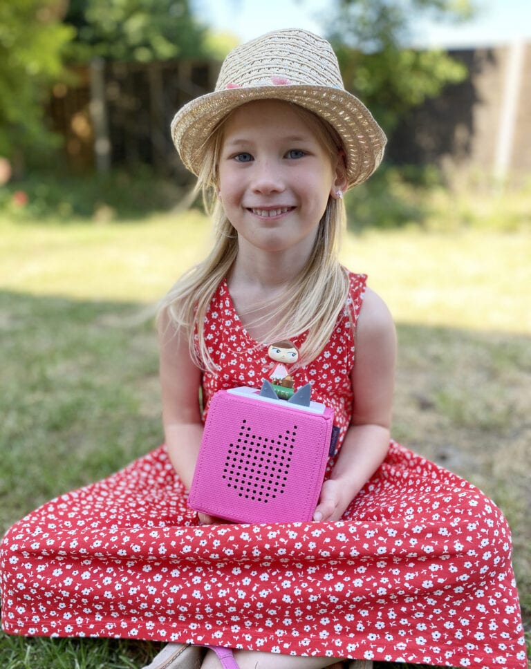 TonieBox Review - Toniebox outside. Aria sitting outside on the grass with a Toniebox on her lap